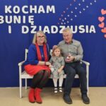 Wnuczka z dziadkami siedzą na ławce - pozują do zdjęcia na 'fotościance'.