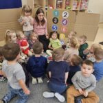 Dzieci wokół nauczyciela przy kartnowej windzie.