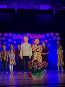 Zdjęcie przedstawia dzieci na scenie podczas recytacji wierszyków. 