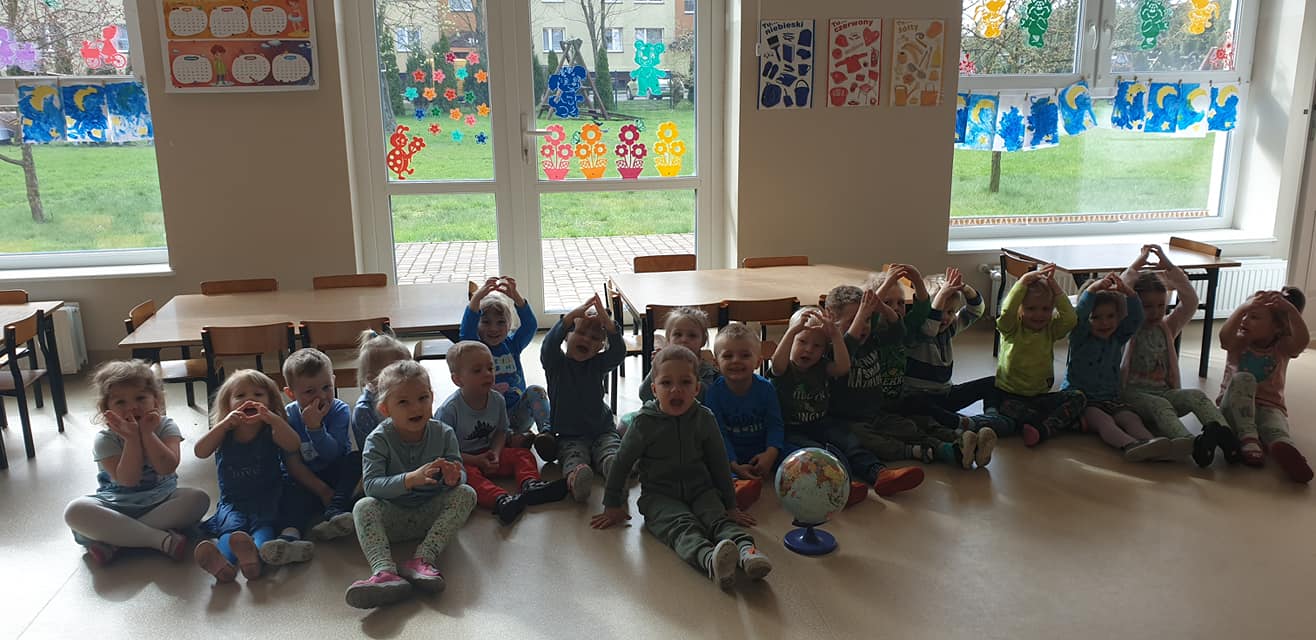 Dzieci z uśmiechem pozują do wspólnego zdjęcia siedząc w grupie obok globusa. Z dłoni próbowały stworzyć serduszko, symbolizujące miłość do naszej planety.