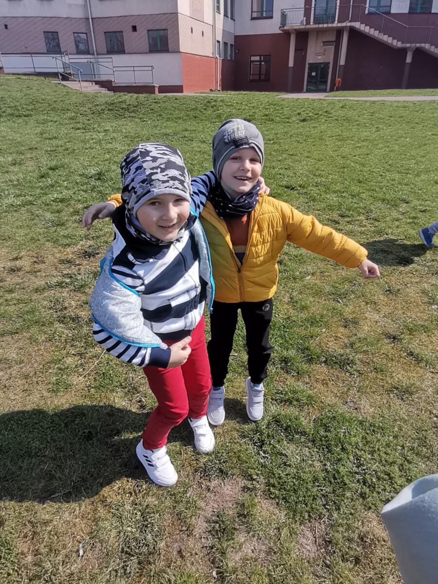 Dwóch chłopców z uśmiechem ba twarzy pozuje do zdjęcia na boisku szkolnym.