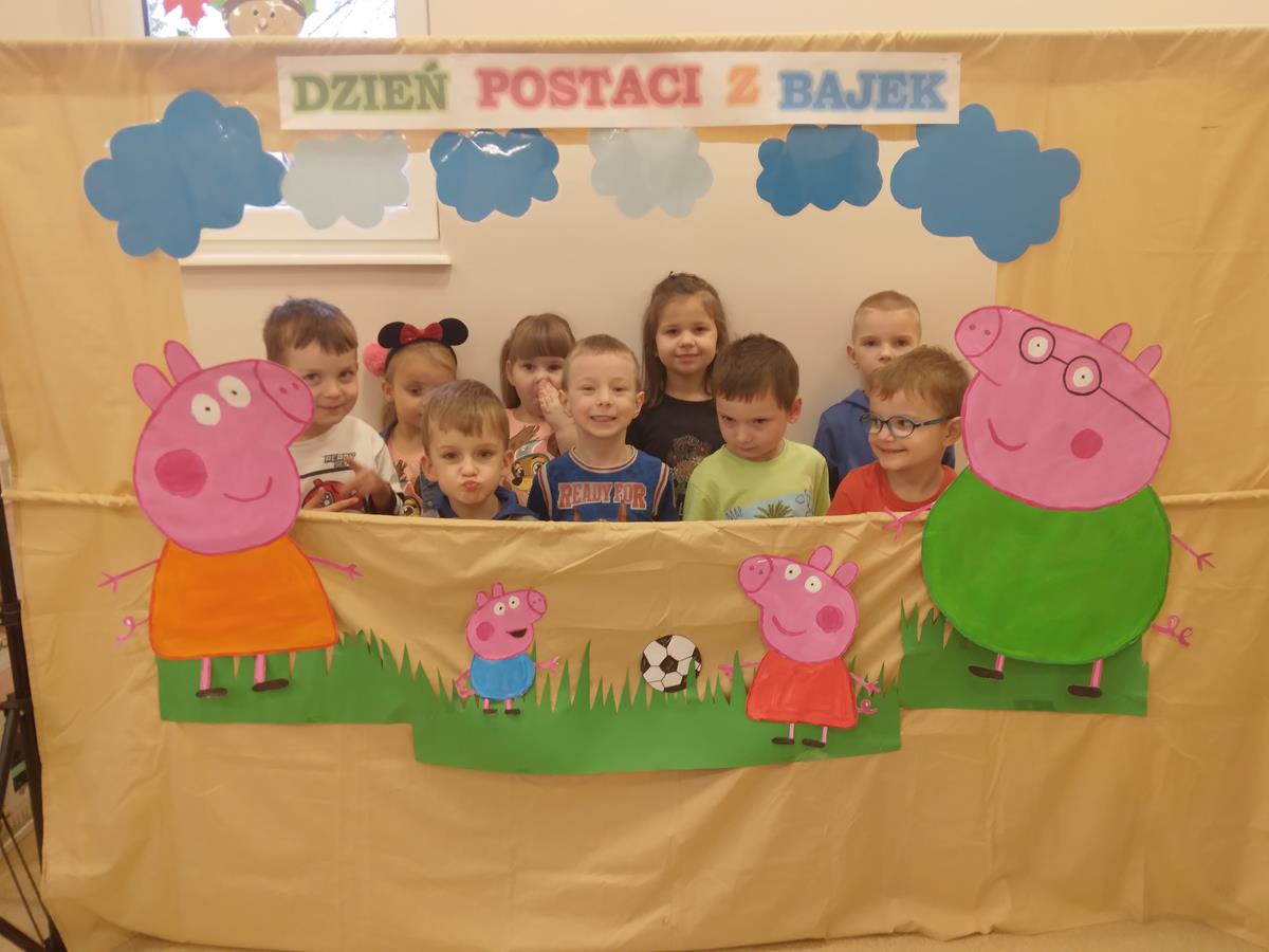 Dzieci pozują do grupowego zdjęcia. Przed nimi ustawiona jest fotobudka, do której przyczepione są postacie z bajki "Świnka Peppa".