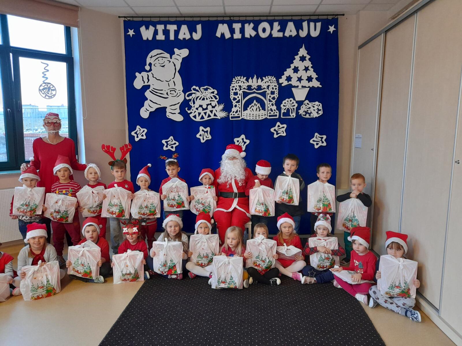 Wspólne zdjęcie z Mikołajem grupy Lwiątka. Dzieci ubrane w mikołajowe czapeczki.