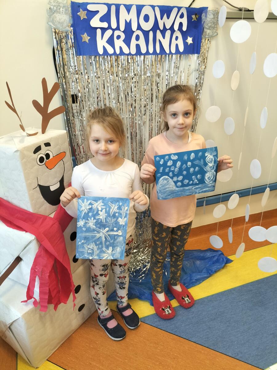 Zdjęcie przedstawia dwie dziewczynki,które prezentują swoje prace plastyczne "Zimowa kraina".