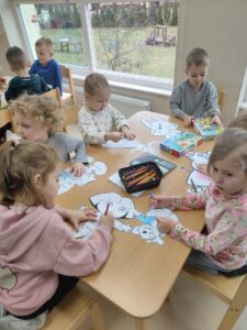 Zdjęcie ukazuje dzieci siedzące przy stole, które kolorują postaci z wybranych baśni i bajek.