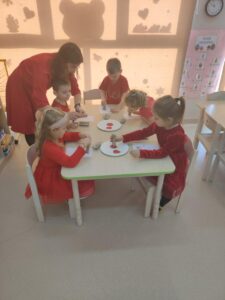 Na zdjęciu widzimy siedzące dzieci przy stoliku. Wykonują one pracę plastyczną - walentynkę dla swoich bliskich.