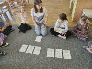 Dzieci siedzą w kole z nauczycielem , a w środku Koła są karty flashcard do rymowanki o jedzeniu.