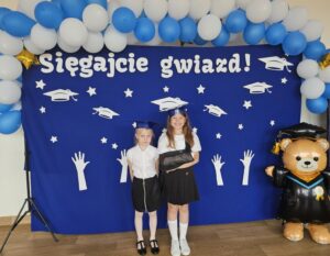 Dziewczyny pozuja do zdjęcia. Stoją przed ścianka ze napisem ' Sięgajcie gwiazd'.
