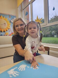 Dziewczynka akceptuje zasady poprzez odciśnięcie swojej rączki pomalowanej białą farbą na brystolu z zasadami.