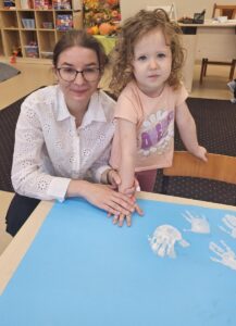 Dziewczynka akceptuje zasady poprzez odciśnięcie swojej rączki pomalowanej białą farbą na brystolu z zasadami.