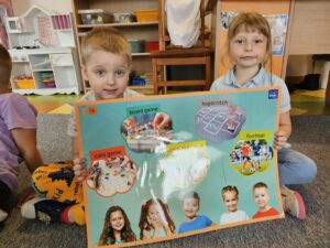 Dwójka dzieci z plakatem prezentującym słownictwo odnośnie gier i zabaw.