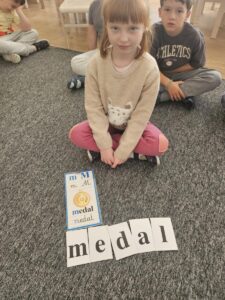 Dziewczynka prezentuje ułożony przez siebie wyraz 'Medal'.