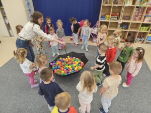 Dzieci podczas zabawy z parasolką i kulkami.