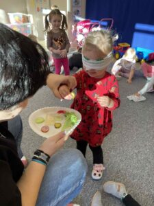 Na zdjeciu widzimy dziecko, które ma przepaskę na oczach. Jej zadaniem jest posmakować warzywo i po smaku powiedzieć jakie to warzywo..