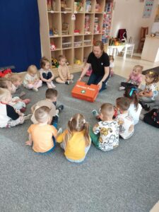 Na zdjęciu widzimy panią wraz z dziecmi siedzącymi w okręgu. Pani pokazuje apteczkę i jej zawartość.