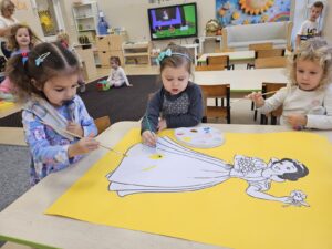 Trzy dziewczynki malują wspólnie farbami Królewnę Śnieżkę.