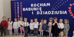 Zdjęcie ukazuje dzieci stojące w rzędzie. Prezentują wierszyk dla babci i dziadka.