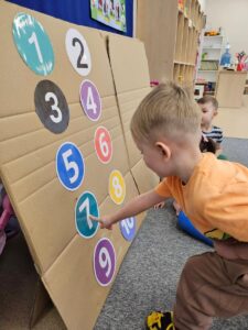 Dziecko uczestniczy w zabawie ruchowej 'Windzie'. Na zdjęciu chłopiec wsjazuje liczbę 7.