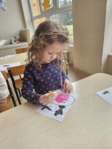 Dziewczynka maluje farbami głowę krowy.